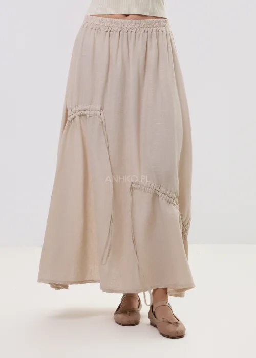 Beżowa spódnica maxi z elastyczną talią i dekoracyjnymi marszczeniami, lekki materiał, asymetryczne przeszycia – stylizacja z balerinami.
