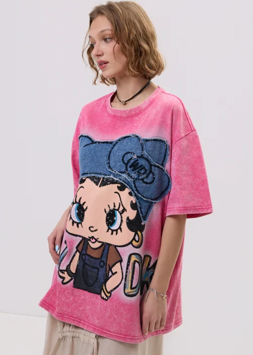Różowy t-shirt damski oversize z nadrukiem postaci i cekinowymi detalami, luźny fason – stylizacja ze spódnicą.