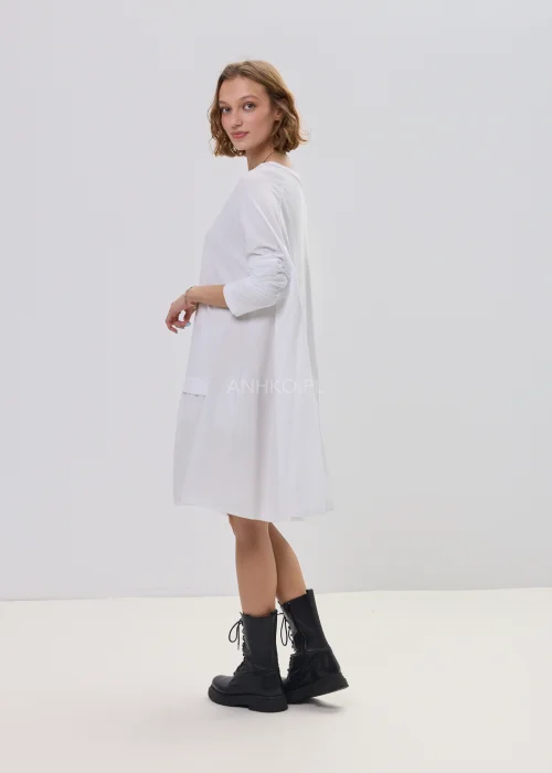 Biała sukienka oversize z falbaną u dołu, asymetryczny krój z dłuższym tyłem, stylizacja z botkami.