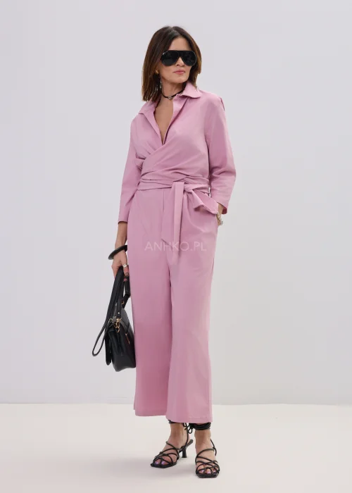 Różowy kombinezon damski z kopertowym dekoltem i wiązaniem w talii, elegancki fason z szerokimi nogawkami, stylizacja z sandałami na obcasie.