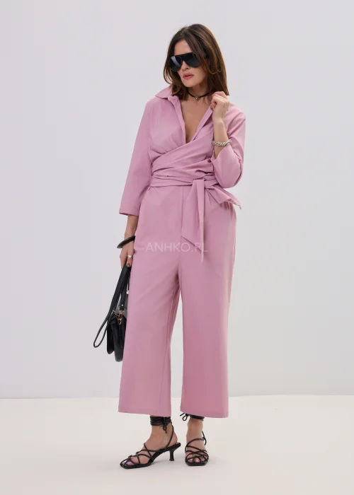 Różowy kombinezon damski z kopertowym dekoltem i wiązaniem w talii, elegancki fason z szerokimi nogawkami, stylizacja z sandałami na obcasie.