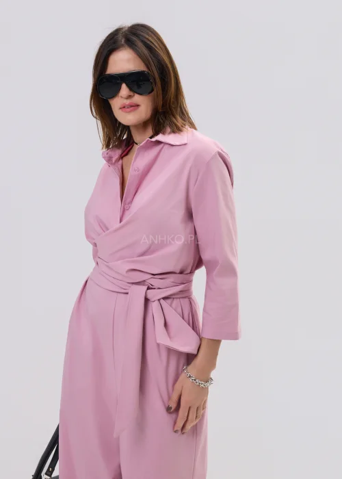 Różowy kombinezon damski z kopertowym dekoltem i wiązaniem w talii, elegancki fason z szerokimi nogawkami, stylizacja z sandałami na obcasie.