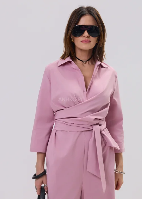 Różowy kombinezon damski z kopertowym dekoltem i wiązaniem w talii, elegancki fason z szerokimi nogawkami, stylizacja z sandałami na obcasie.