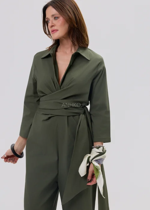 Oliwkowy kombinezon damski z kopertowym dekoltem i wiązaniem w talii, szerokie nogawki, elegancka stylizacja z sandałami.