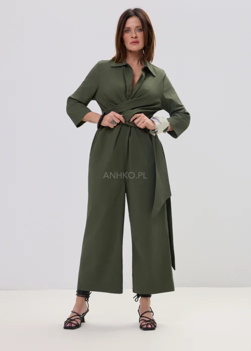 Oliwkowy kombinezon damski z kopertowym dekoltem i wiązaniem w talii, szerokie nogawki, elegancka stylizacja z sandałami.