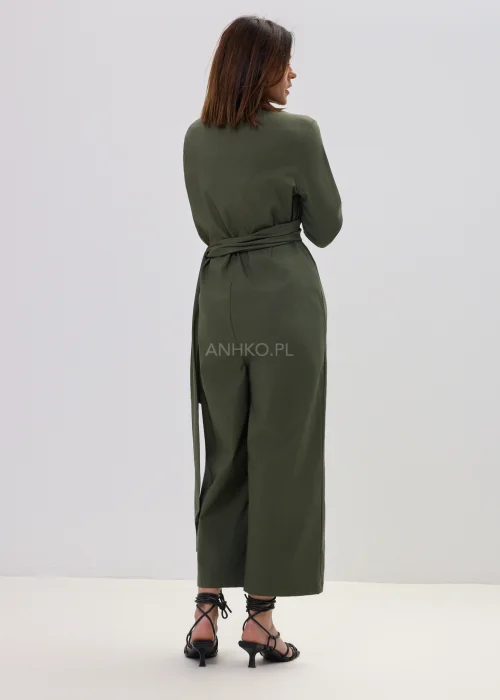 Oliwkowy kombinezon damski z kopertowym dekoltem i wiązaniem w talii, szerokie nogawki, elegancka stylizacja z sandałami.