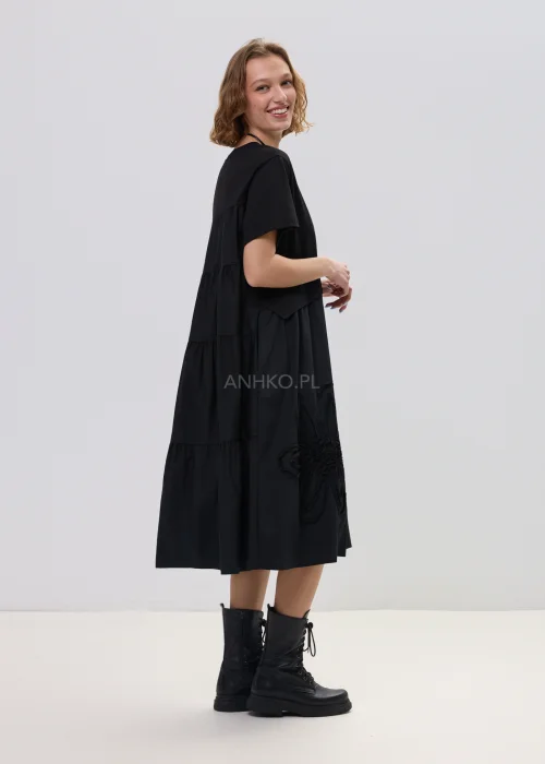 Czarna sukienka midi o luźnym fasonie z krótkim rękawem i ozdobnym detalem kwiatowym, minimalistyczny styl – stylizacja z botkami.