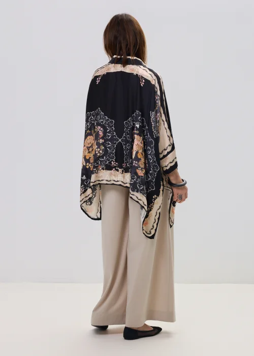 Czarna koszula oversize z dekoracyjnym printem w stylu vintage, szerokie rękawy typu kimono i kontrastowe wzory – stylizacja z jasnymi, eleganckimi spodniami.