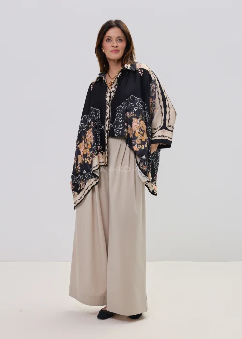 Czarna koszula oversize z dekoracyjnym printem w stylu vintage, szerokie rękawy typu kimono i kontrastowe wzory – stylizacja z jasnymi, eleganckimi spodniami.