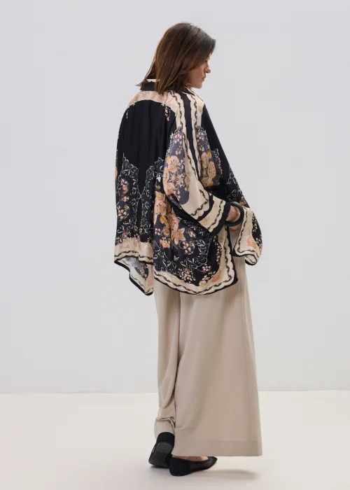 Czarna koszula oversize z dekoracyjnym printem w stylu vintage, szerokie rękawy typu kimono i kontrastowe wzory – stylizacja z jasnymi, eleganckimi spodniami.