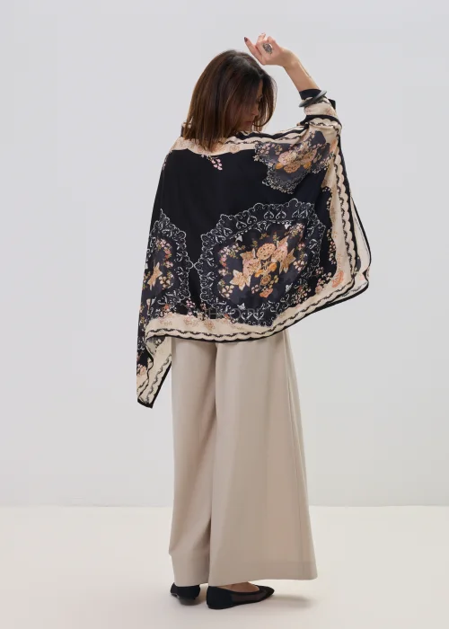 Czarna koszula oversize z dekoracyjnym printem w stylu vintage, szerokie rękawy typu kimono i kontrastowe wzory – stylizacja z jasnymi, eleganckimi spodniami.