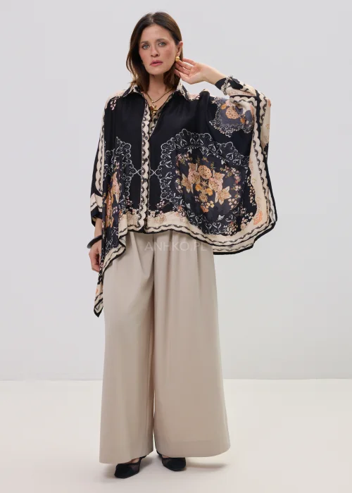 Czarna koszula oversize z dekoracyjnym printem w stylu vintage, szerokie rękawy typu kimono i kontrastowe wzory – stylizacja z jasnymi, eleganckimi spodniami.