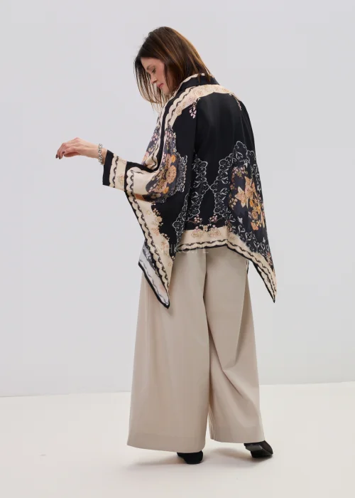 Czarna koszula oversize z dekoracyjnym printem w stylu vintage, szerokie rękawy typu kimono i kontrastowe wzory – stylizacja z jasnymi, eleganckimi spodniami.
