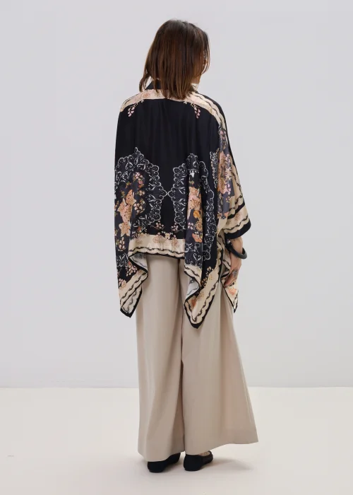 Czarna koszula oversize z dekoracyjnym printem w stylu vintage, szerokie rękawy typu kimono i kontrastowe wzory – stylizacja z jasnymi, eleganckimi spodniami.
