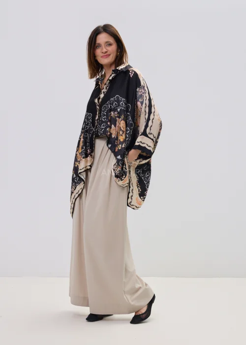 Czarna koszula oversize z dekoracyjnym printem w stylu vintage, szerokie rękawy typu kimono i kontrastowe wzory – stylizacja z jasnymi, eleganckimi spodniami.
