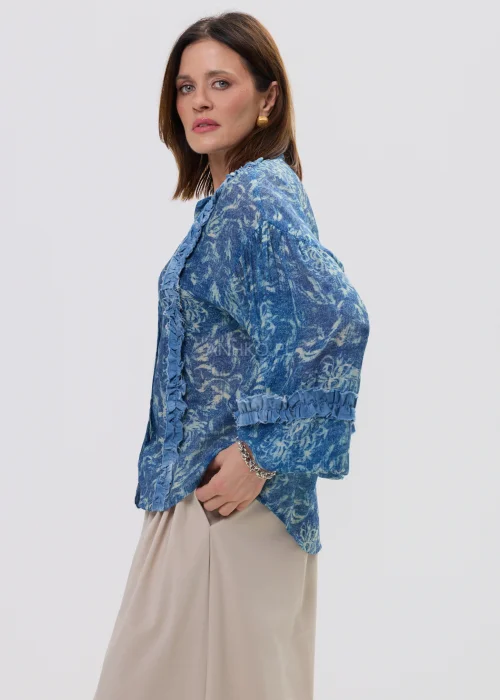 Niebieska koszula damska oversize z printem i falbankami, zapinana na guziki, lekki materiał w stylowej, casualowej stylizacji.