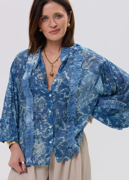 Niebieska koszula damska oversize z printem i falbankami, zapinana na guziki, lekki materiał w stylowej, casualowej stylizacji.