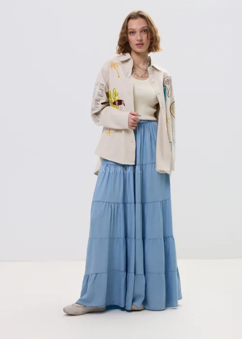 Niebieska spódnica maxi z elastyczną talią i falbanami, lekki, rozkloszowany fason w kobiecej stylizacji.