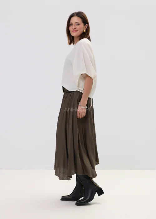 Spódnica midi brązowa o zwiewnym, asymetrycznym kroju z delikatnym połyskiem, stylizowana z szerokim paskiem z ozdobną klamrą i botkami na obcasie.