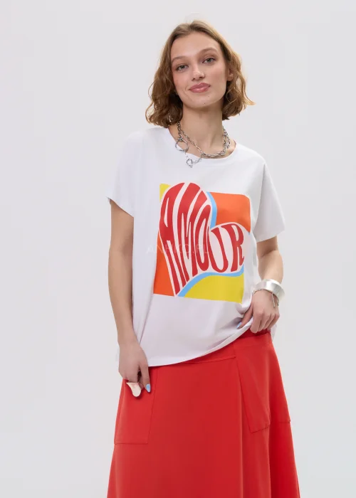 T-shirt oversize biały z kolorowym printem „Amour” w formie serca, luźny fason z krótkim rękawem – casualowa stylizacja z czerwono-pomarańczową spódnicą.