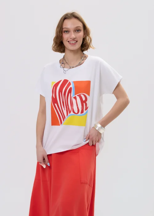 T-shirt oversize biały z kolorowym printem „Amour” w formie serca, luźny fason z krótkim rękawem – casualowa stylizacja z czerwono-pomarańczową spódnicą.