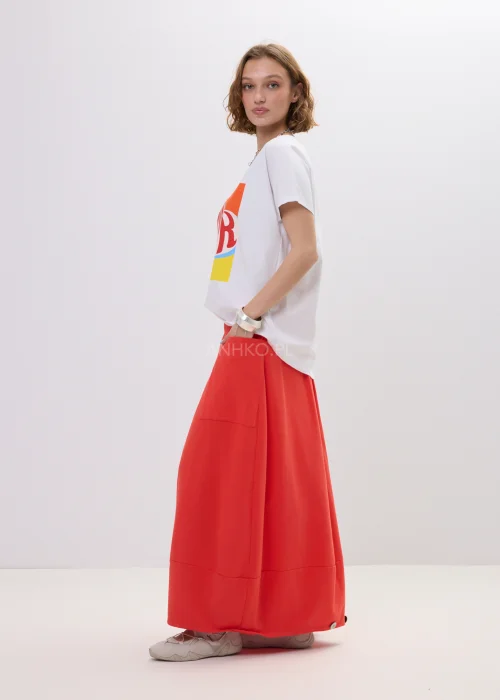 T-shirt oversize biały z kolorowym printem „Amour” w formie serca, luźny fason z krótkim rękawem – casualowa stylizacja z czerwono-pomarańczową spódnicą.