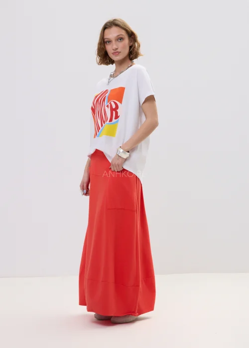 T-shirt oversize biały z kolorowym printem „Amour” w formie serca, luźny fason z krótkim rękawem – casualowa stylizacja z czerwono-pomarańczową spódnicą.