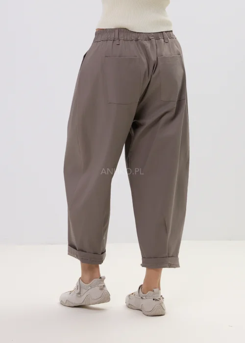 Spodnie damskie o luźnym kroju w kolorze taupe, z elastyczną talią i podwiniętymi nogawkami, ozdobione designerskim brelokiem – komfortowy model do codziennych stylizacji.