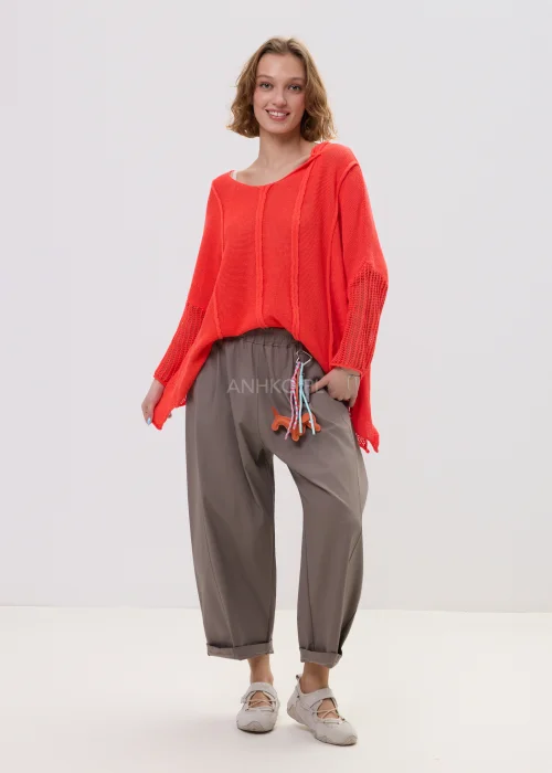 Sweter damski o luźnym kroju w intensywnym koralowym kolorze, z ażurowymi rękawami i obniżoną linią ramion, lekki i stylowy element codziennych stylizacji.