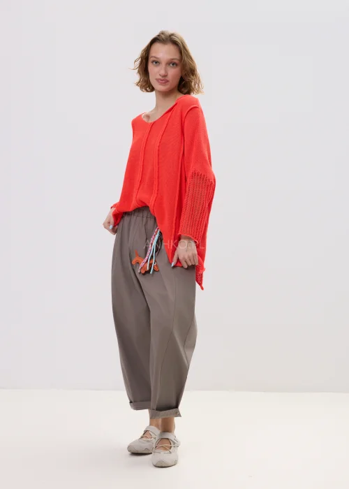 Sweter damski o luźnym kroju w intensywnym koralowym kolorze, z ażurowymi rękawami i obniżoną linią ramion, lekki i stylowy element codziennych stylizacji.