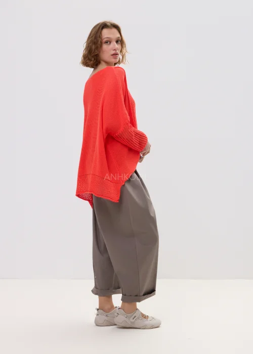 Sweter damski o luźnym kroju w intensywnym koralowym kolorze, z ażurowymi rękawami i obniżoną linią ramion, lekki i stylowy element codziennych stylizacji.