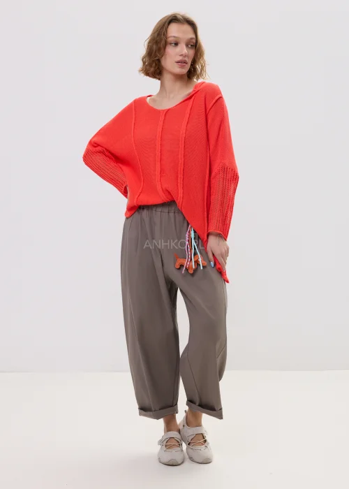 Sweter damski o luźnym kroju w intensywnym koralowym kolorze, z ażurowymi rękawami i obniżoną linią ramion, lekki i stylowy element codziennych stylizacji.