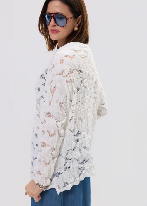 Biała bluzka damska z koronkową strukturą i długim rękawem, lekko transparentny materiał, styl casual.