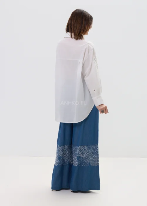 Biała koszula damska z haftowaną aplikacją róży, luźny fason, lekko transparentny materiał, elegancki styl.