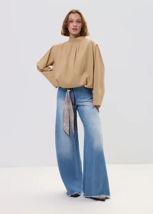 Beżowa bluzka damska oversize z wysoką stójką i szerokimi rękawami, minimalistyczny fason zestawiony z jasnymi jeansami w casualowej stylizacji.