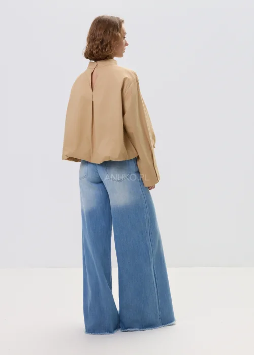 Beżowa bluzka damska oversize z wysoką stójką i szerokimi rękawami, minimalistyczny fason zestawiony z jasnymi jeansami w casualowej stylizacji.