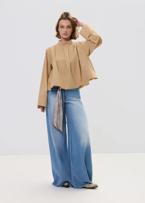Beżowa bluzka damska oversize z wysoką stójką i szerokimi rękawami, minimalistyczny fason zestawiony z jasnymi jeansami w casualowej stylizacji.