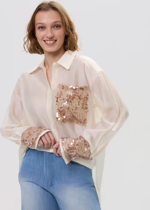 Beżowa koszula damska z cekinową kieszenią i mankietami, luźny fason, lekko transparentny materiał, styl casual-elegant.