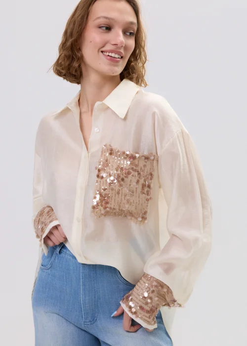 Beżowa koszula damska z cekinową kieszenią i mankietami, luźny fason, lekko transparentny materiał, styl casual-elegant.