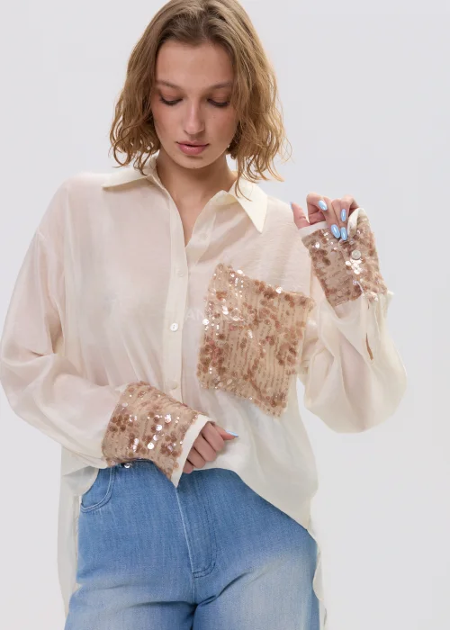 Beżowa koszula damska z cekinową kieszenią i mankietami, luźny fason, lekko transparentny materiał, styl casual-elegant.