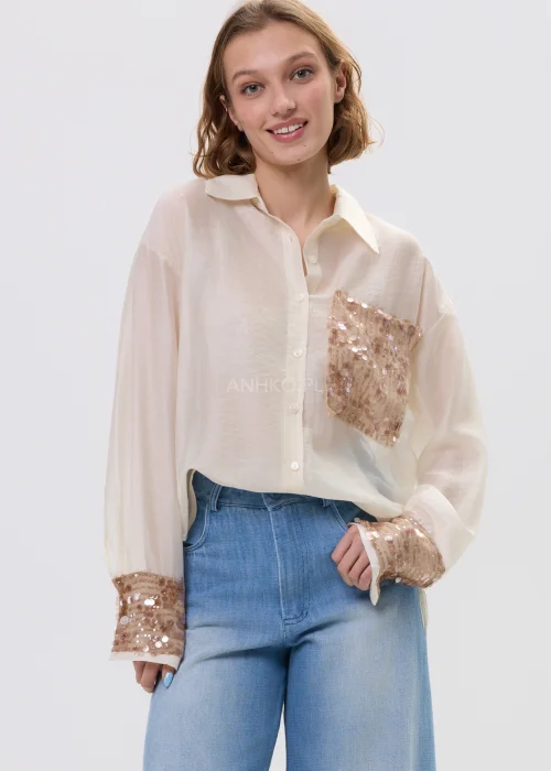 Beżowa koszula damska z cekinową kieszenią i mankietami, luźny fason, lekko transparentny materiał, styl casual-elegant.