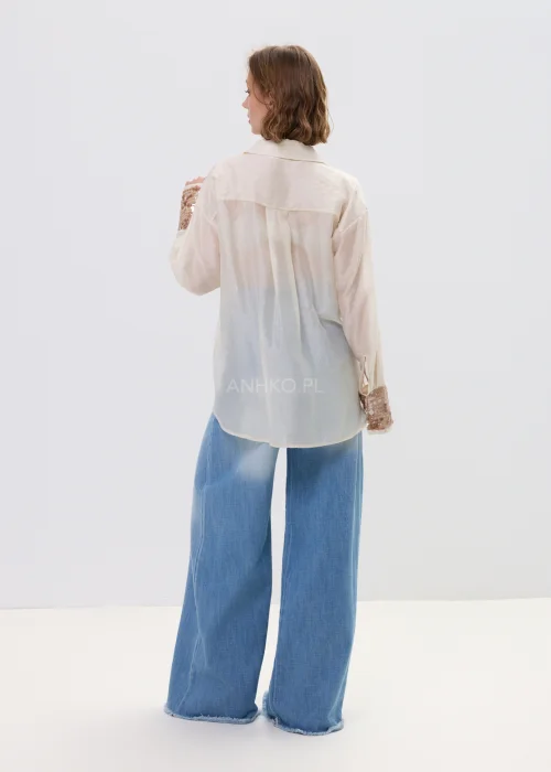 Beżowa koszula damska z cekinową kieszenią i mankietami, luźny fason, lekko transparentny materiał, styl casual-elegant.