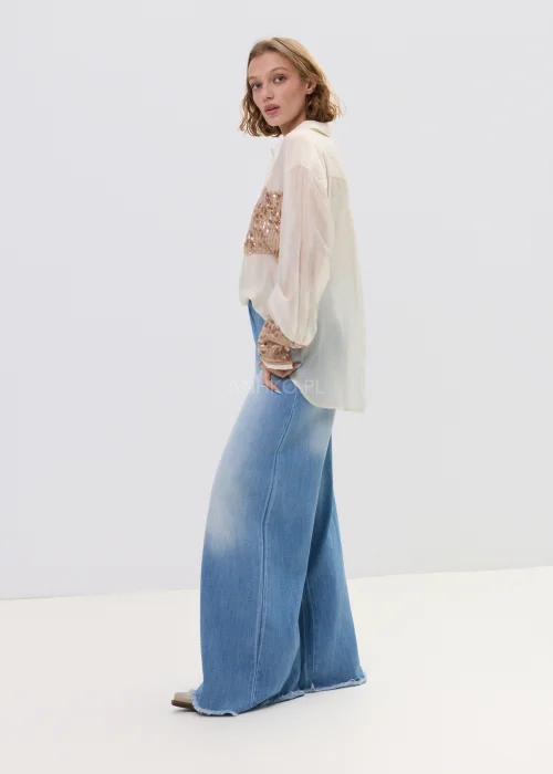 Beżowa koszula damska z cekinową kieszenią i mankietami, luźny fason, lekko transparentny materiał, styl casual-elegant.