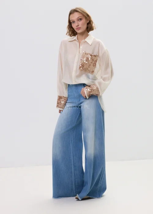 Beżowa koszula damska z cekinową kieszenią i mankietami, luźny fason, lekko transparentny materiał, styl casual-elegant.