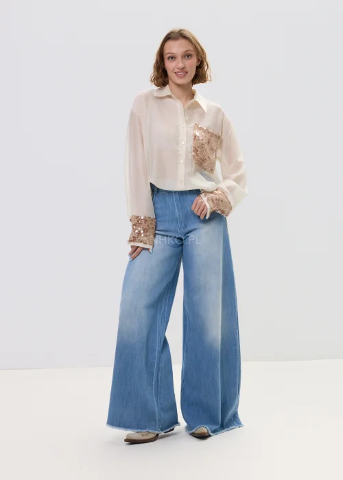 Beżowa koszula damska z cekinową kieszenią i mankietami, luźny fason, lekko transparentny materiał, styl casual-elegant.