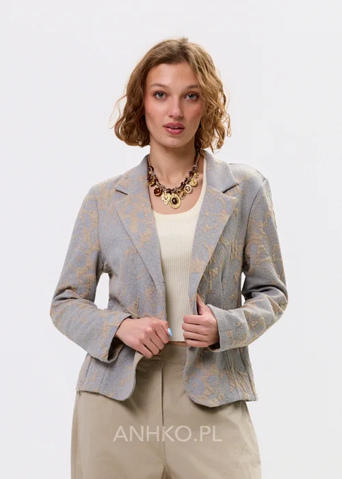 Beżowo-szary żakiet damski w delikatny roślinny wzór, zapinany na guziki, z klasycznymi klapami i prostym fasonem. Elegancka marynarka w stylu smart casual zestawiona z jasnymi spodniami cargo.