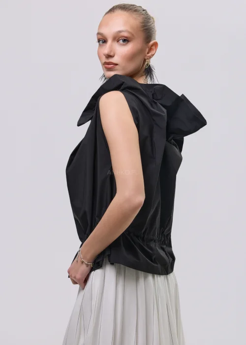 Czarna bluzka damska bez rękawów z ozdobnym marszczeniem przy dekolcie i regulacją w talii, zestawiona z plisowaną spódnicą.