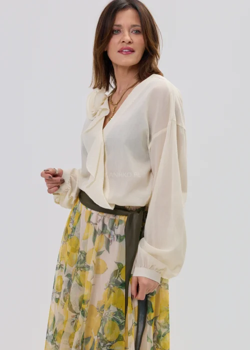 Kremowa bluzka damska z kopertowym dekoltem i ozdobną aplikacją kwiatową na ramieniu, o lekkim, zwiewnym materiale i eleganckim fasonie.