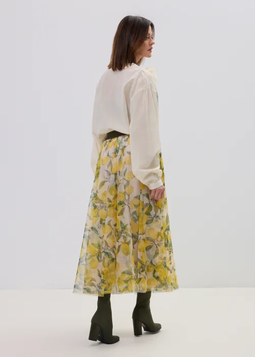 Kremowa bluzka damska z kopertowym dekoltem i ozdobną aplikacją kwiatową na ramieniu, o lekkim, zwiewnym materiale i eleganckim fasonie.