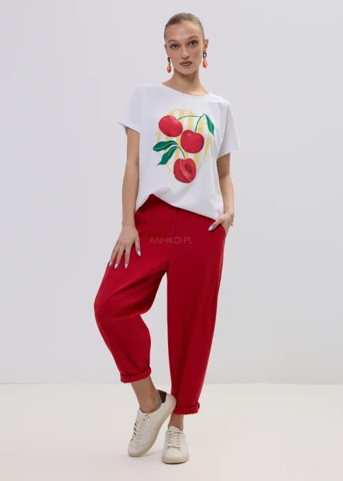 Biały t-shirt damski z kolorowym nadrukiem wiśni, luźny fason, zestawiony z czerwonymi spodniami.